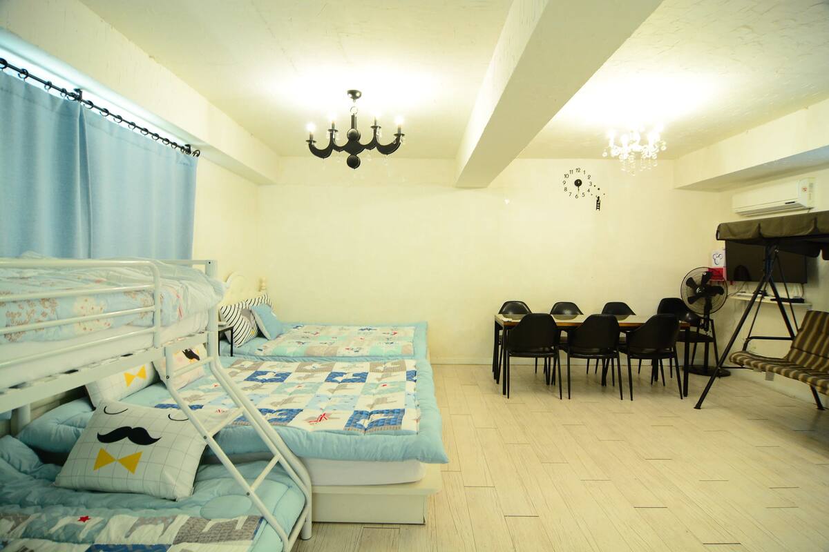 A room with bunk beds, a dining table with chairs, a chandelier, and a clock on the wall.