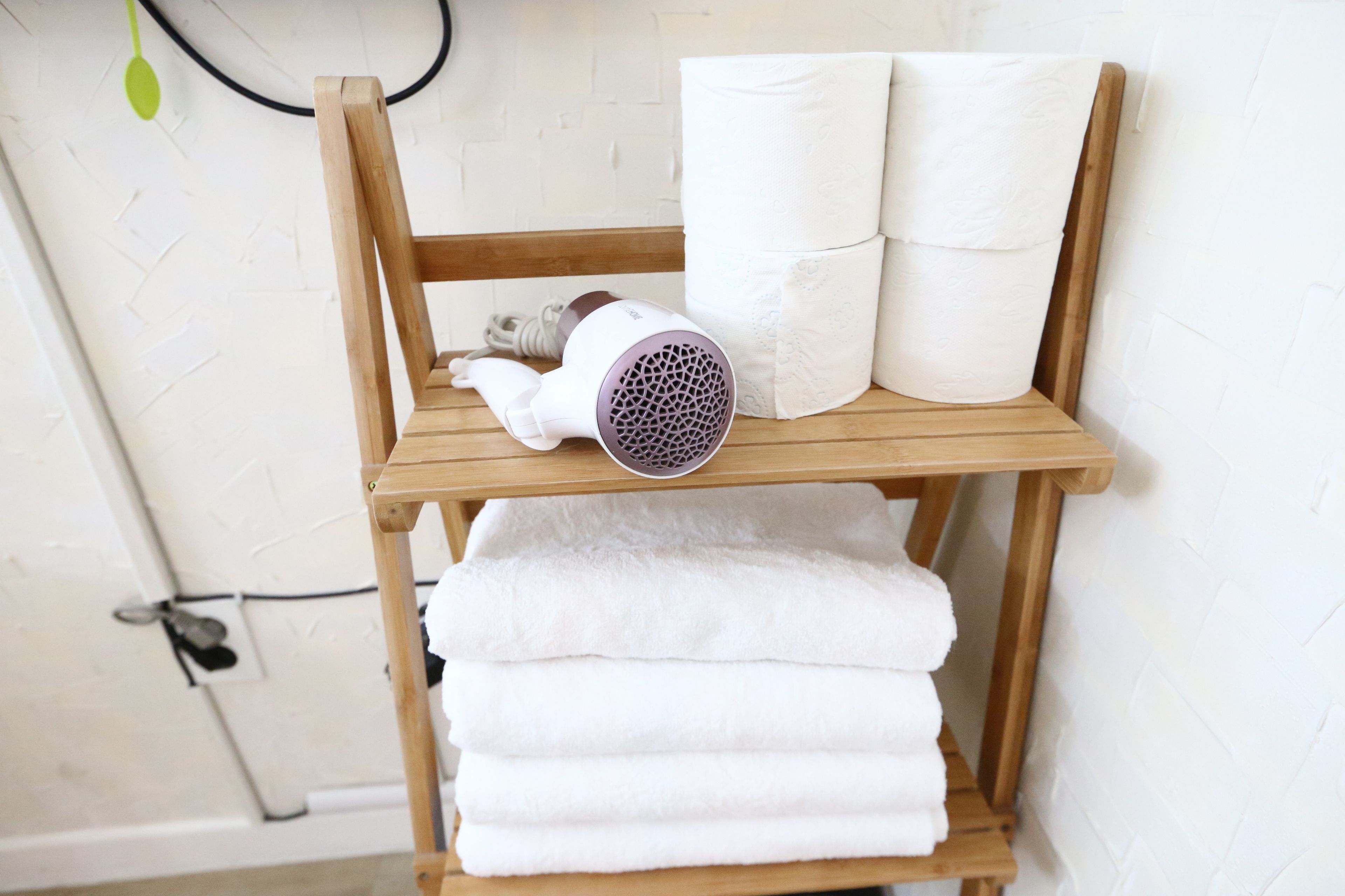 A wooden shelf with a hairdryer and rolled towels.