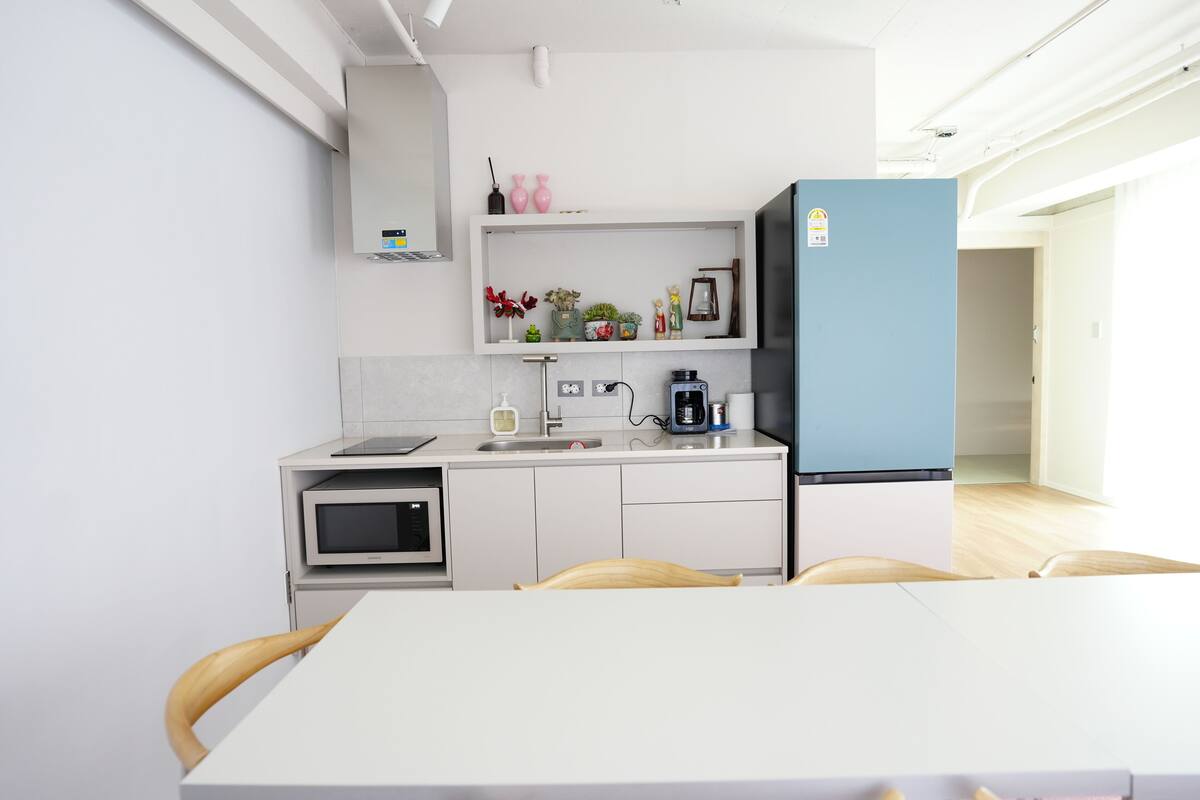 A modern kitchen with white cabinets, a microwave, a coffee machine, and a blue refrigerator.