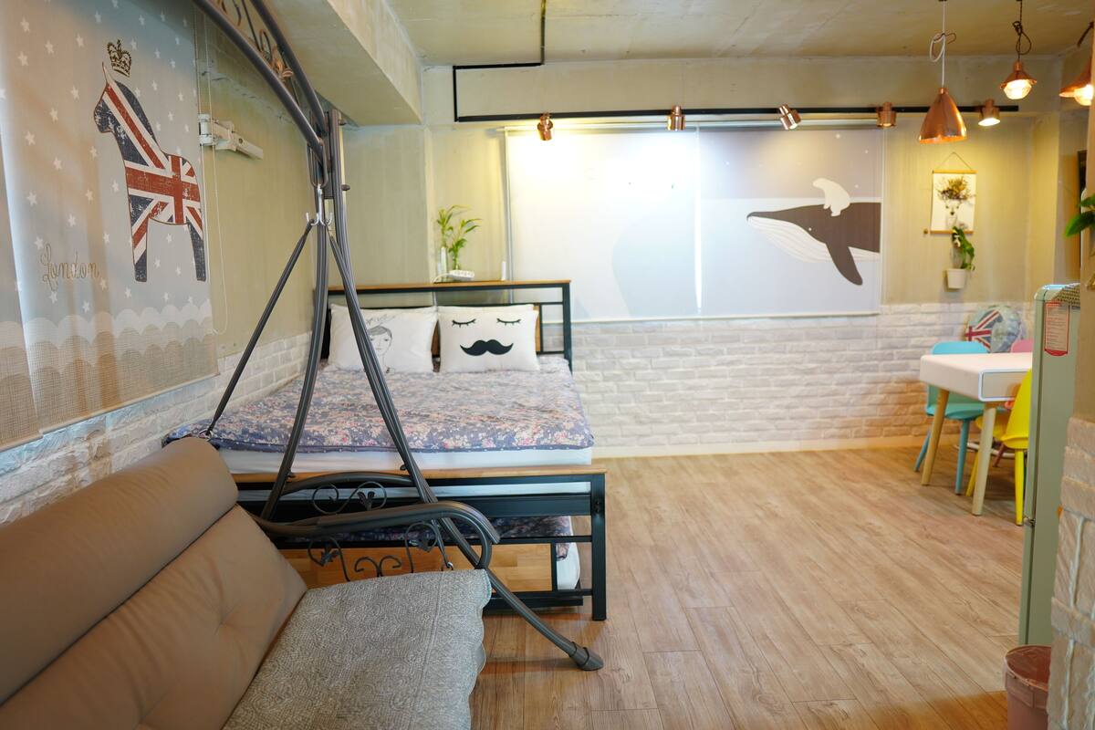 A room with a bed, a sofa, a desk, and a wall with a British flag and a whale mural.