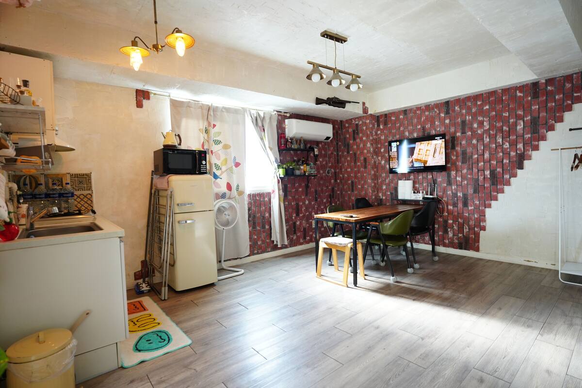 A compact kitchen with a refrigerator, microwave, and sink. There's a dining area with a table and chairs, and a TV mounted on the wall.