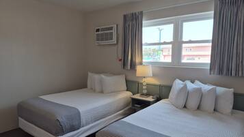 A hotel room with two beds, a nightstand, a lamp, an air conditioning unit, and a window with curtains.