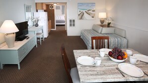 A hotel room with a dining table set for two, a bed with a view, a kitchenette, and a bathroom visible through an open door. - Aquarius Oceanfront Inn (Wildwood)