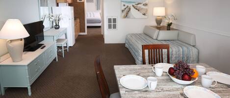 A hotel room with a dining table set for two, a bed with a view, a kitchenette, and a bathroom visible through an open door.