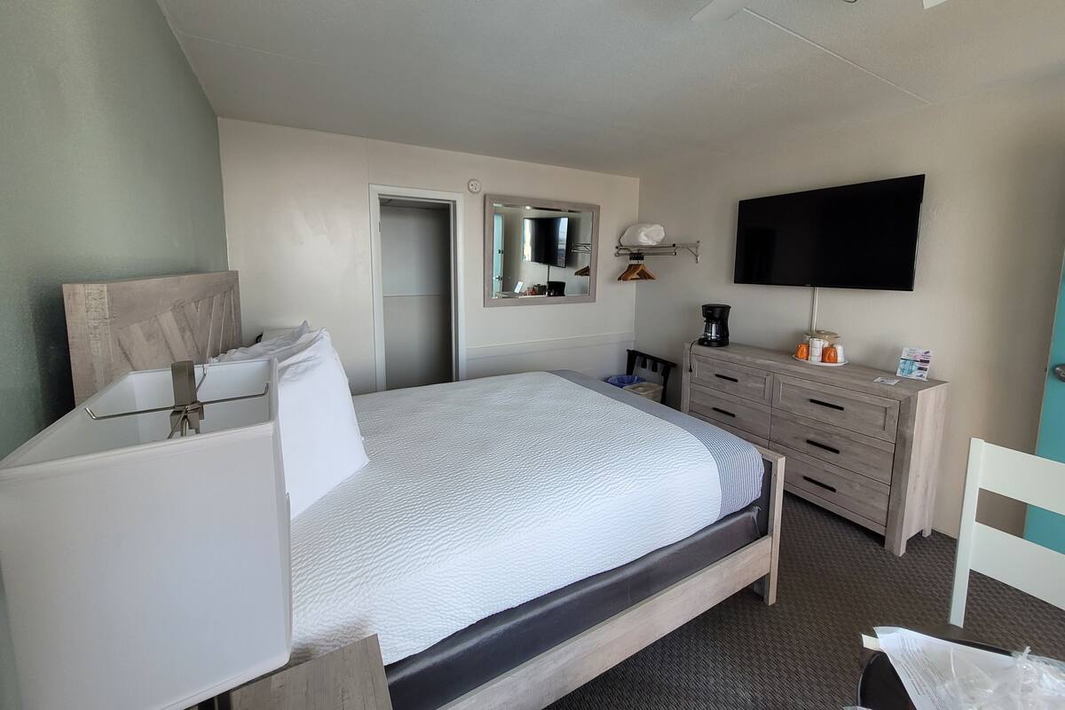 A hotel room with a bed, a dresser, a television, and a mirror.