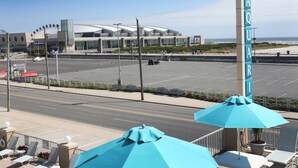 A parking lot with a large building in the background, a sign with the letters "AQUARIUM," and outdoor seating with umbrellas. - Aquarius Oceanfront Inn (Wildwood)