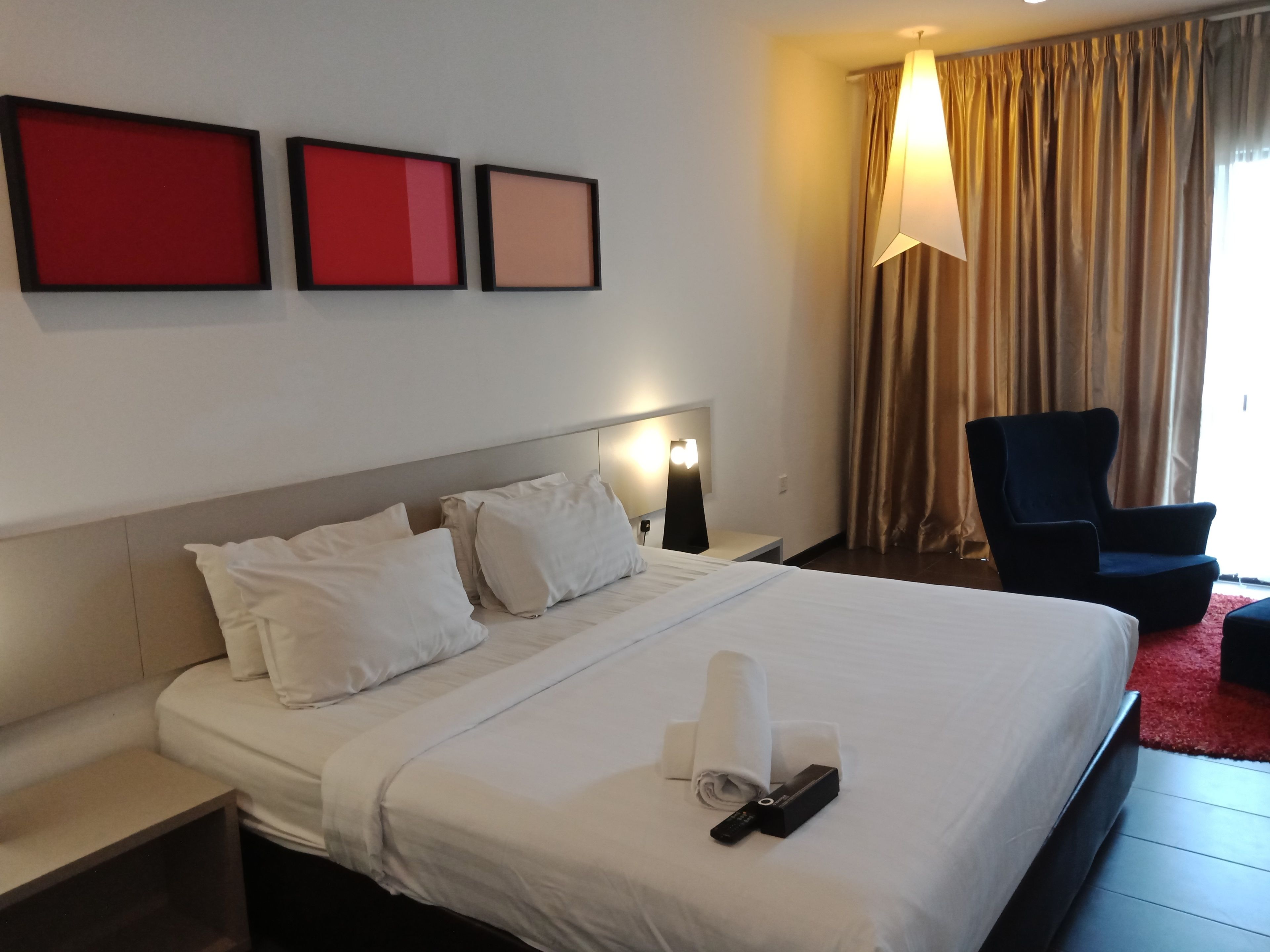 A hotel room with a large bed, white bedding, a nightstand with a lamp, and a chair.