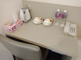 A hotel room desk with a tissue box, a coffee maker, two cups, two bottles of water, and a telephone.