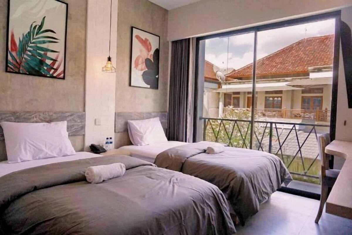 A hotel room with two beds, a balcony with a view, and artwork on the walls.