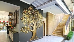 A modern interior with a large golden tree mural, a staircase, and a reception area with a counter and shelves. - Gemini Star Hotel Kuta (Kuta)