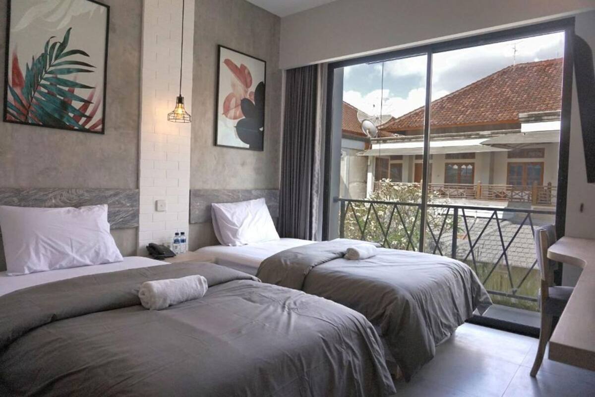A hotel room with two beds, a balcony, and a view of a building with a tiled roof.