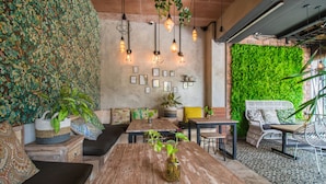 A cozy cafe with wooden tables and chairs, a green wall with plants, and hanging pendant lights. - Gemini Star Hotel Kuta (Kuta)