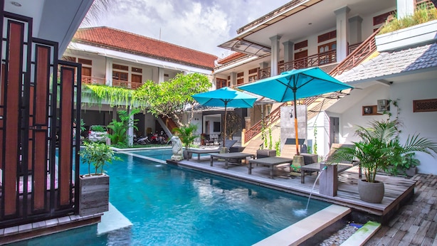 A swimming pool with a wooden deck, lounge chairs, and potted plants. - Gemini Star Hotel Kuta (Kuta)