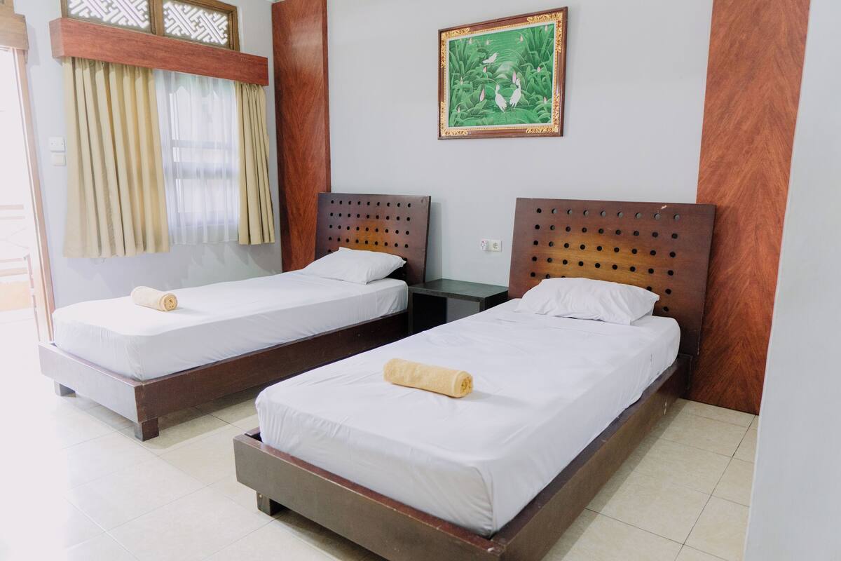 Two single beds with wooden headboards, a small table, and a wall-mounted picture.
