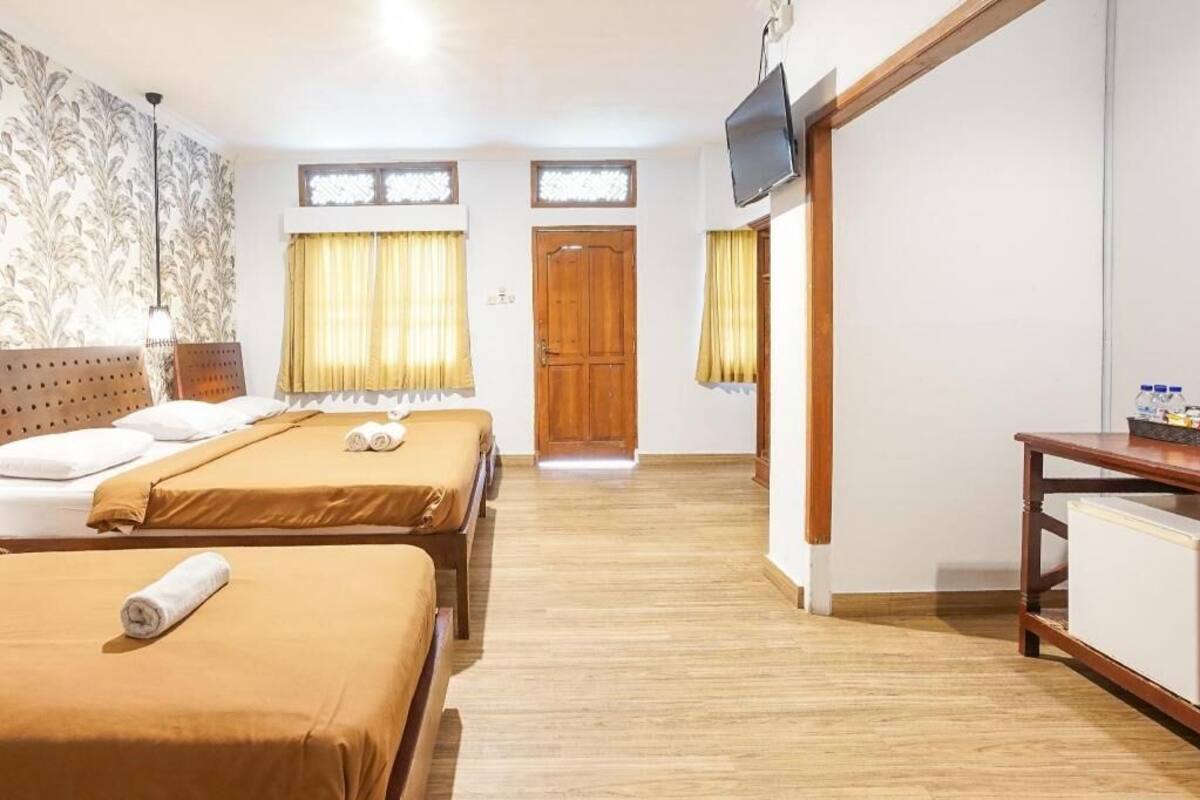 A hotel room with two beds, a TV, a wooden door, and a small table.