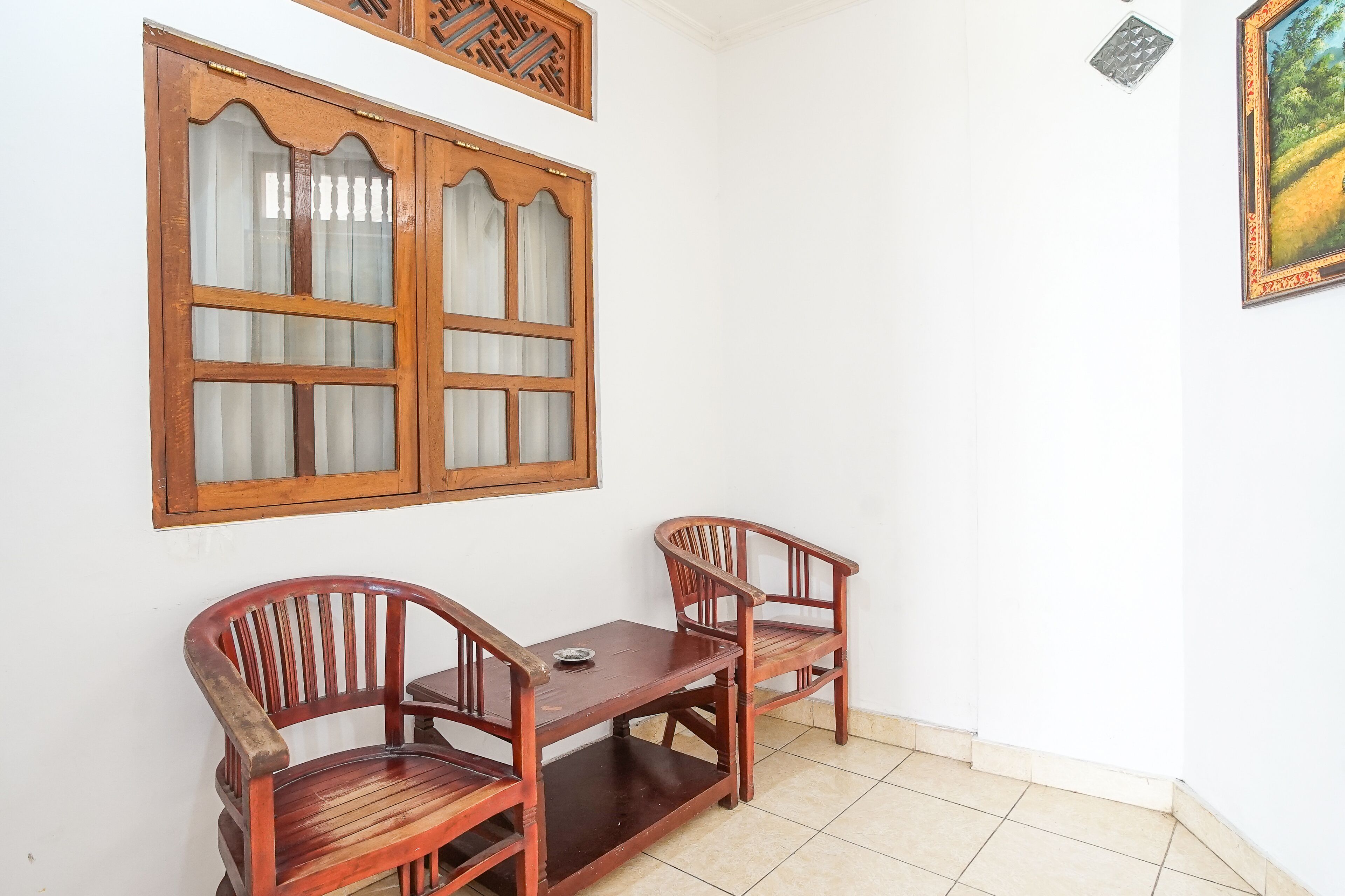 A room with a wooden table and two chairs, a window with decorative woodwork, and a framed picture on the wall.