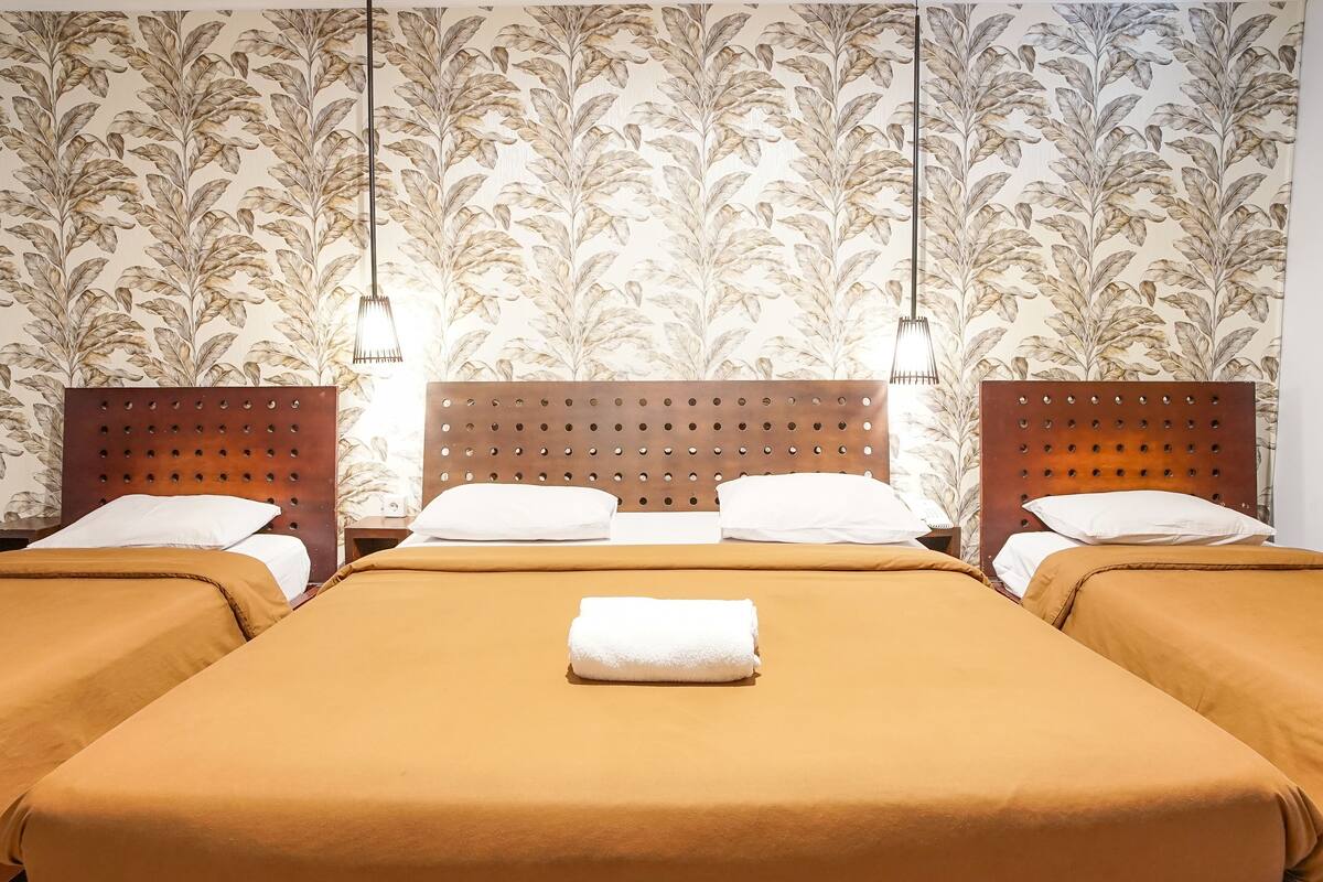 A hotel room with three beds, each with a wooden headboard and white bedding.