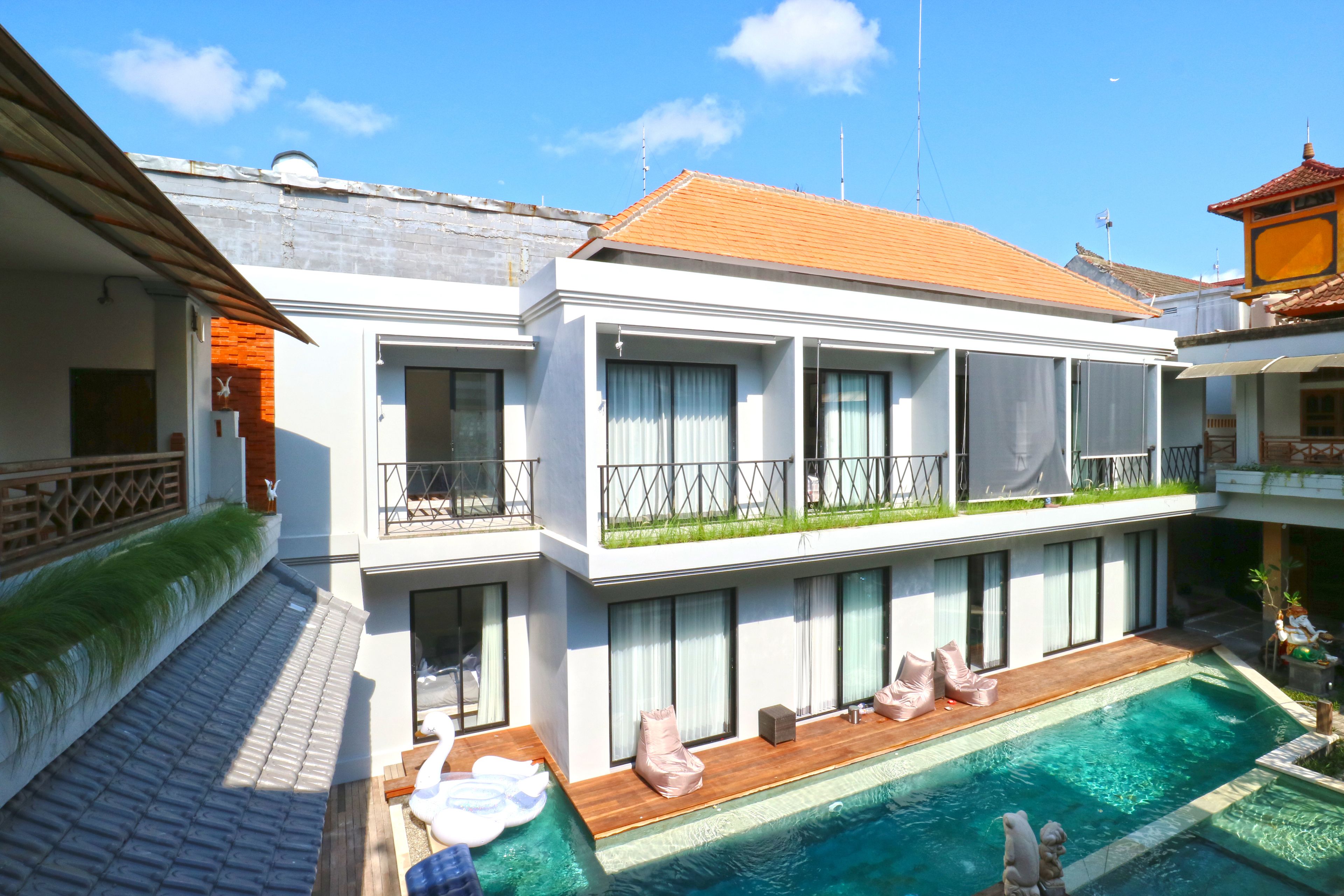 A modern two-story building with a swimming pool, large windows, and a balcony with outdoor seating.