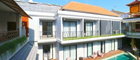 A modern two-story building with a swimming pool, large windows, and a balcony with outdoor seating.