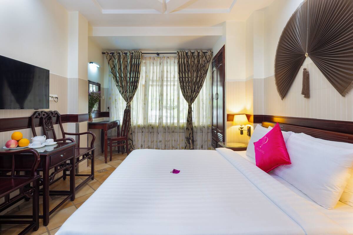 A hotel room with a bed, a desk with chairs, a television, and curtains.