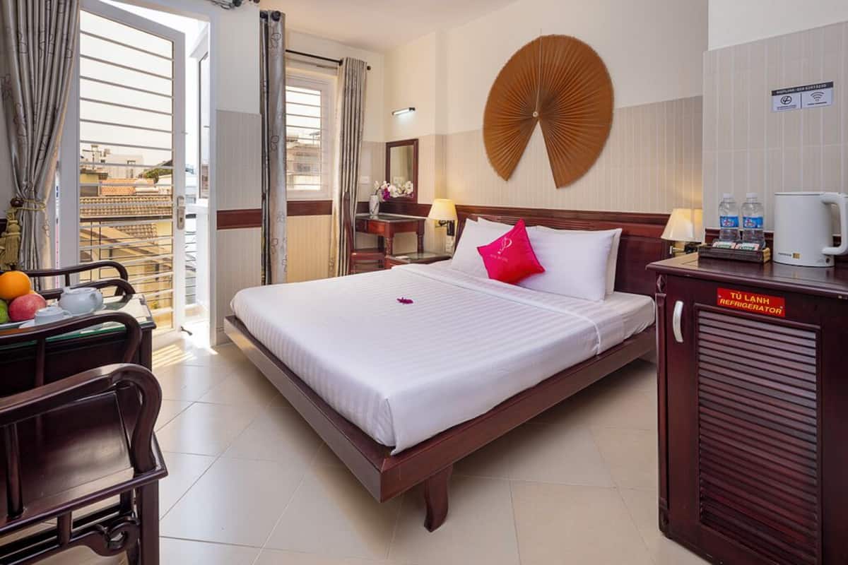 A hotel room with a bed, a desk with a chair, a minibar, and a view through a door.