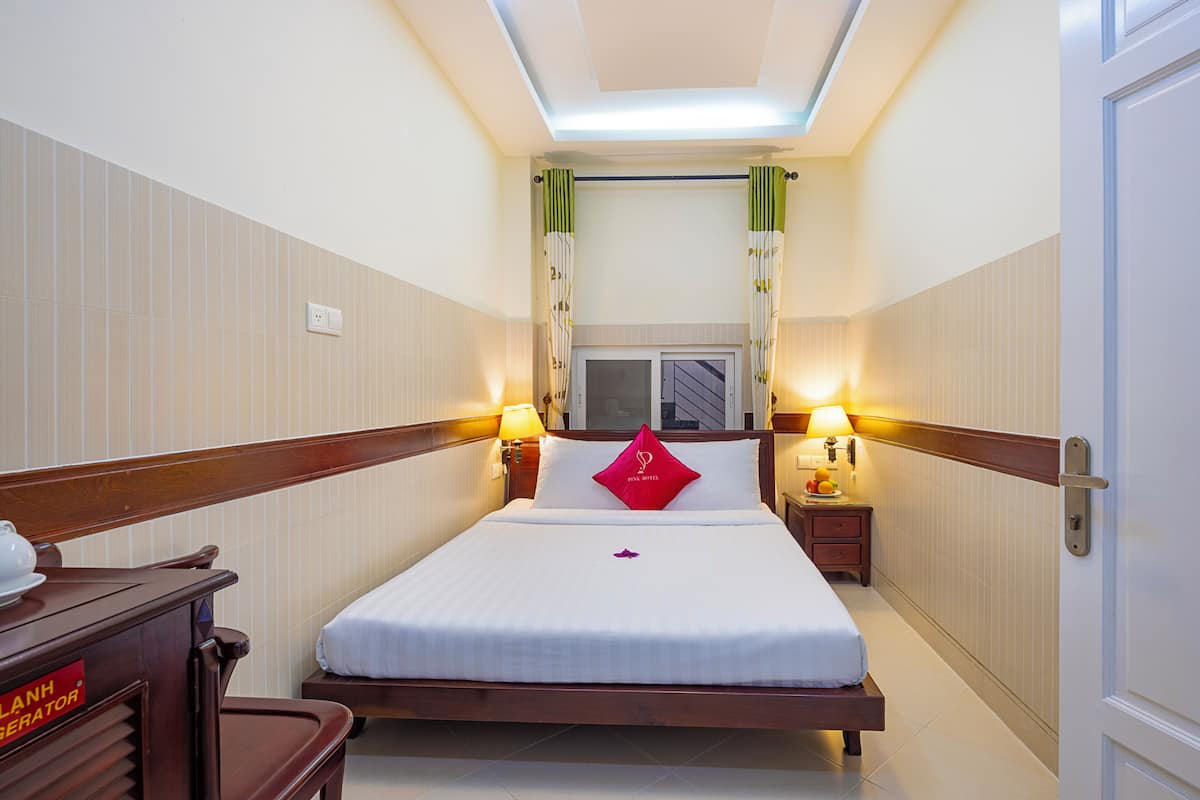 A hotel room with a bed, bedside lamps, a nightstand, and a wooden bench.