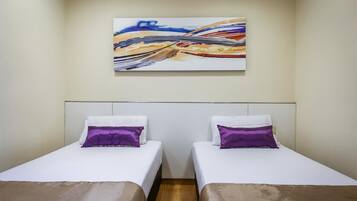 Een kamer met twee bedden, elk voorzien van een witte matras en een paars kussen. Boven de bedden hangt een schilderij aan de muur.
