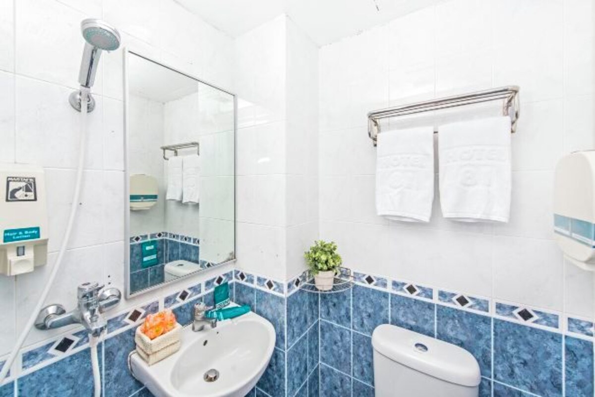 A modern bathroom with a white sink, a mirror, a shower, and a toilet. There are two towels hanging on a rack and a small potted plant on the counter.