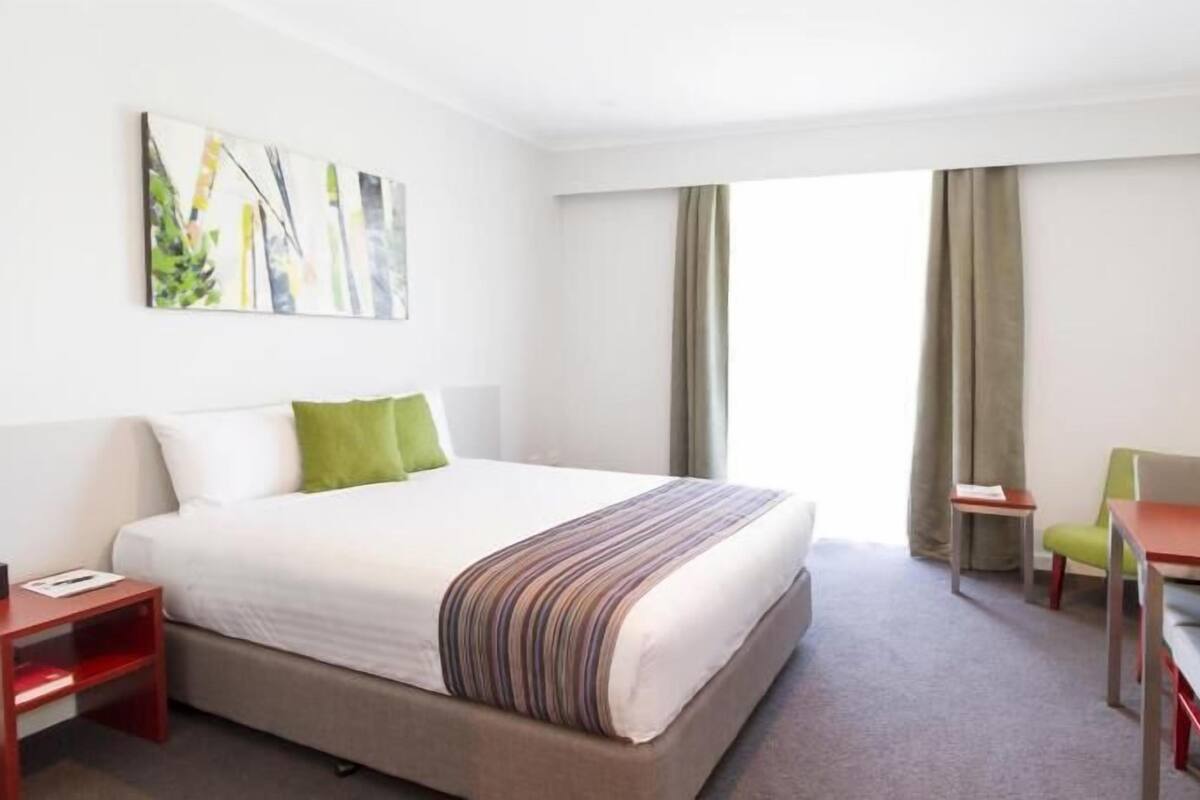 Habitación de hotel con cama, escritorio, silla, televisor y un cuadro en la pared.
