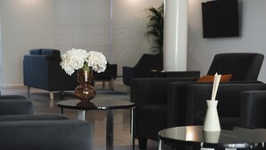 Zona d'estar moderna amb sofàs negres, una taula rodona amb un ram de flors i un televisor negre penjat a la paret.
