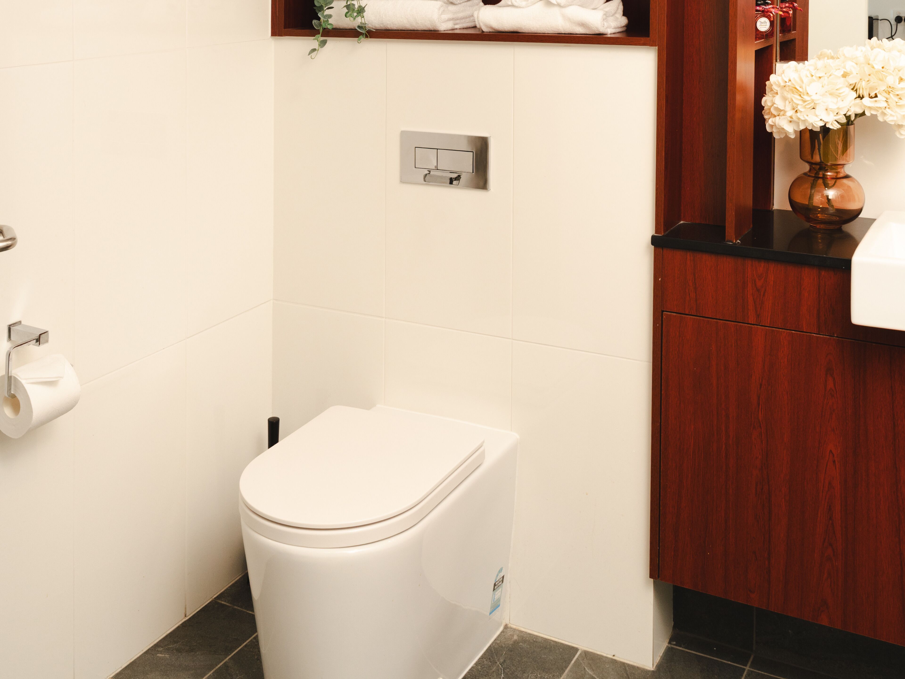 Une salle de bain équipée de toilettes, d’un porte-serviettes, d’un miroir et d’un vase avec des fleurs.