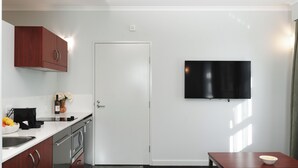 Eine Küche mit einer weißen Tür, einem flachbildfernseher an der Wand und einem Holztisch mit einer Schüssel.