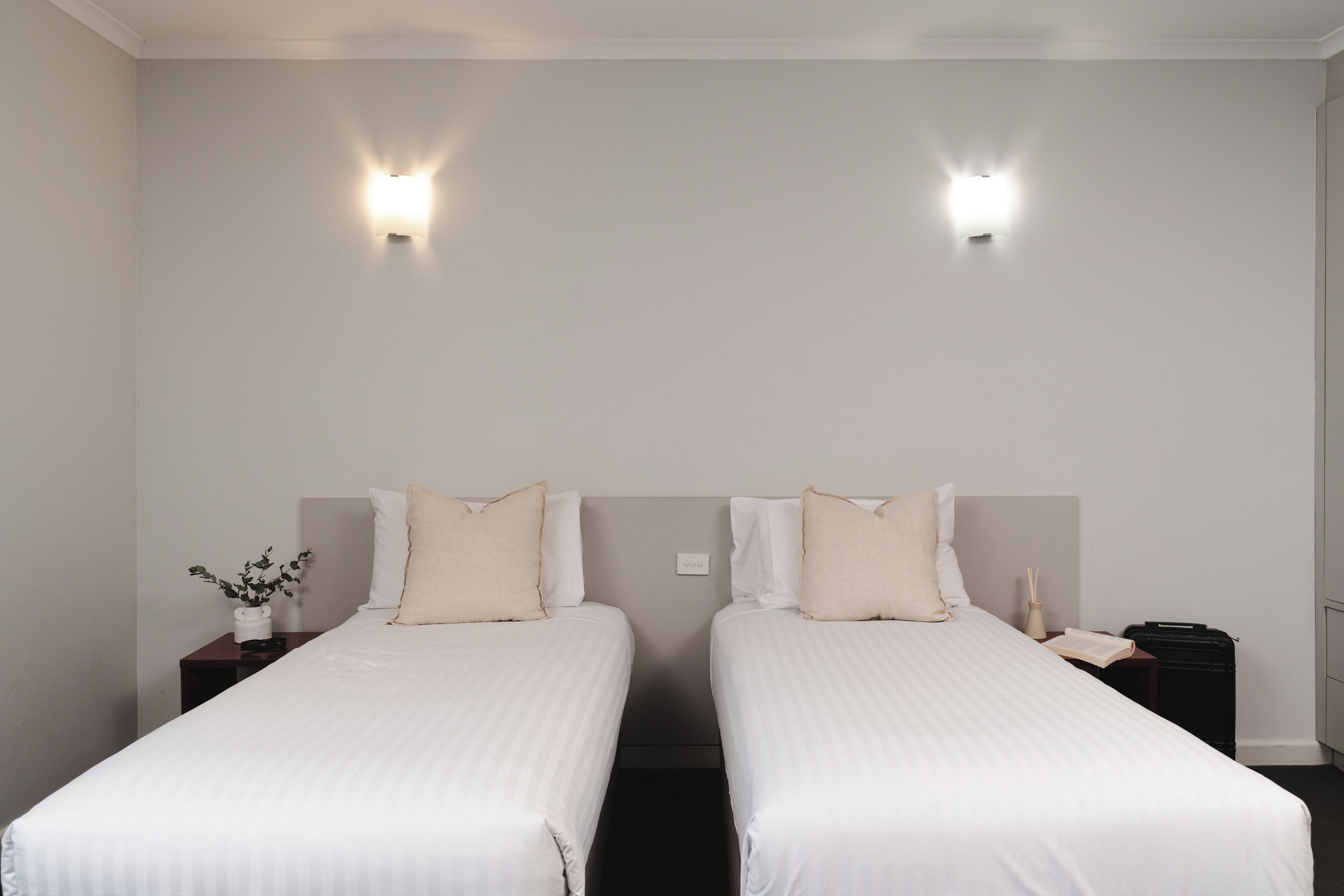 Ein Doppelzimmer mit zwei Betten, Nachttischen, Wandleuchten und einer kleinen Pflanze.