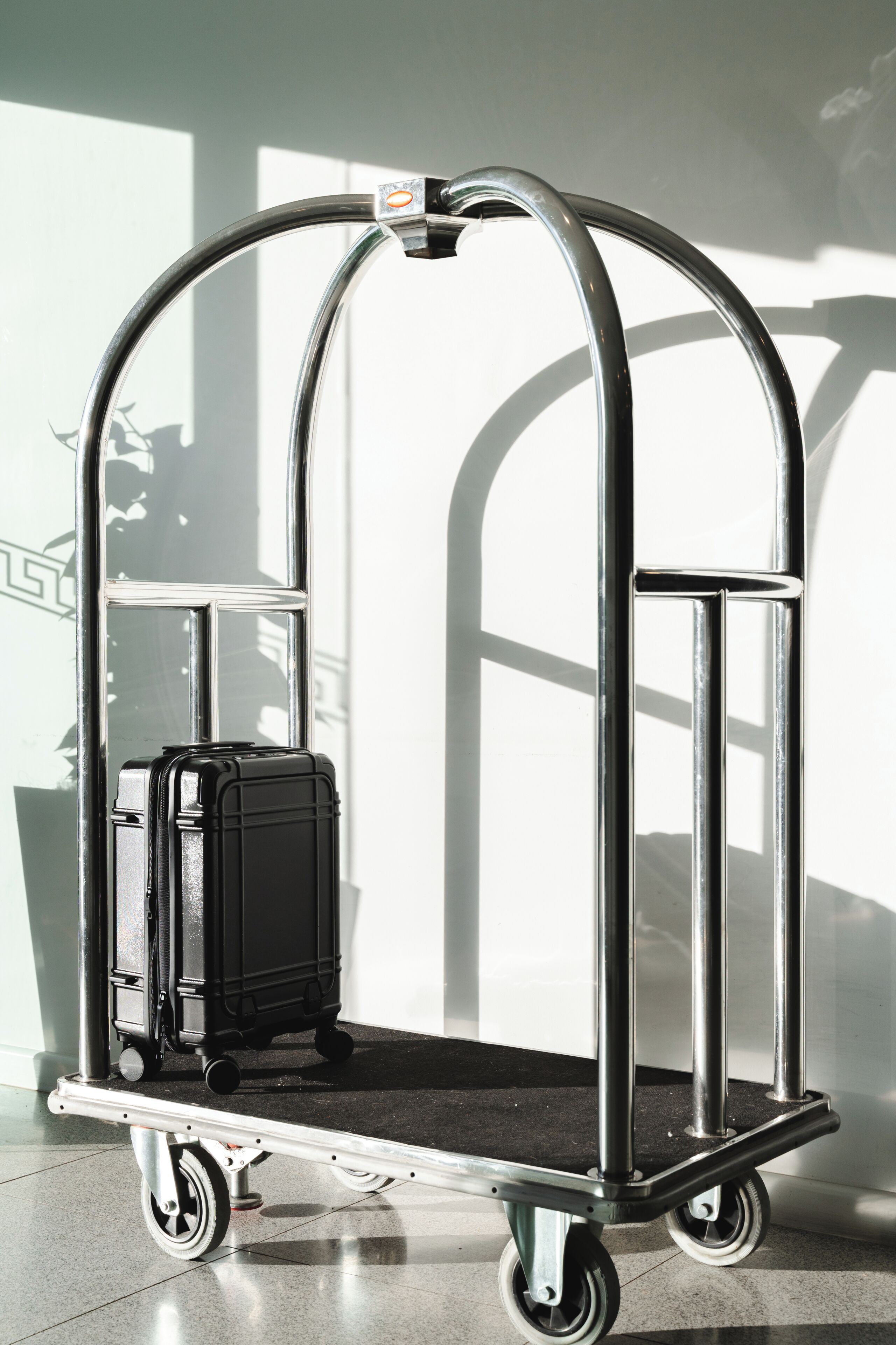 A metallic luggage cart with wheels, a handle, and a small rectangular object on top.