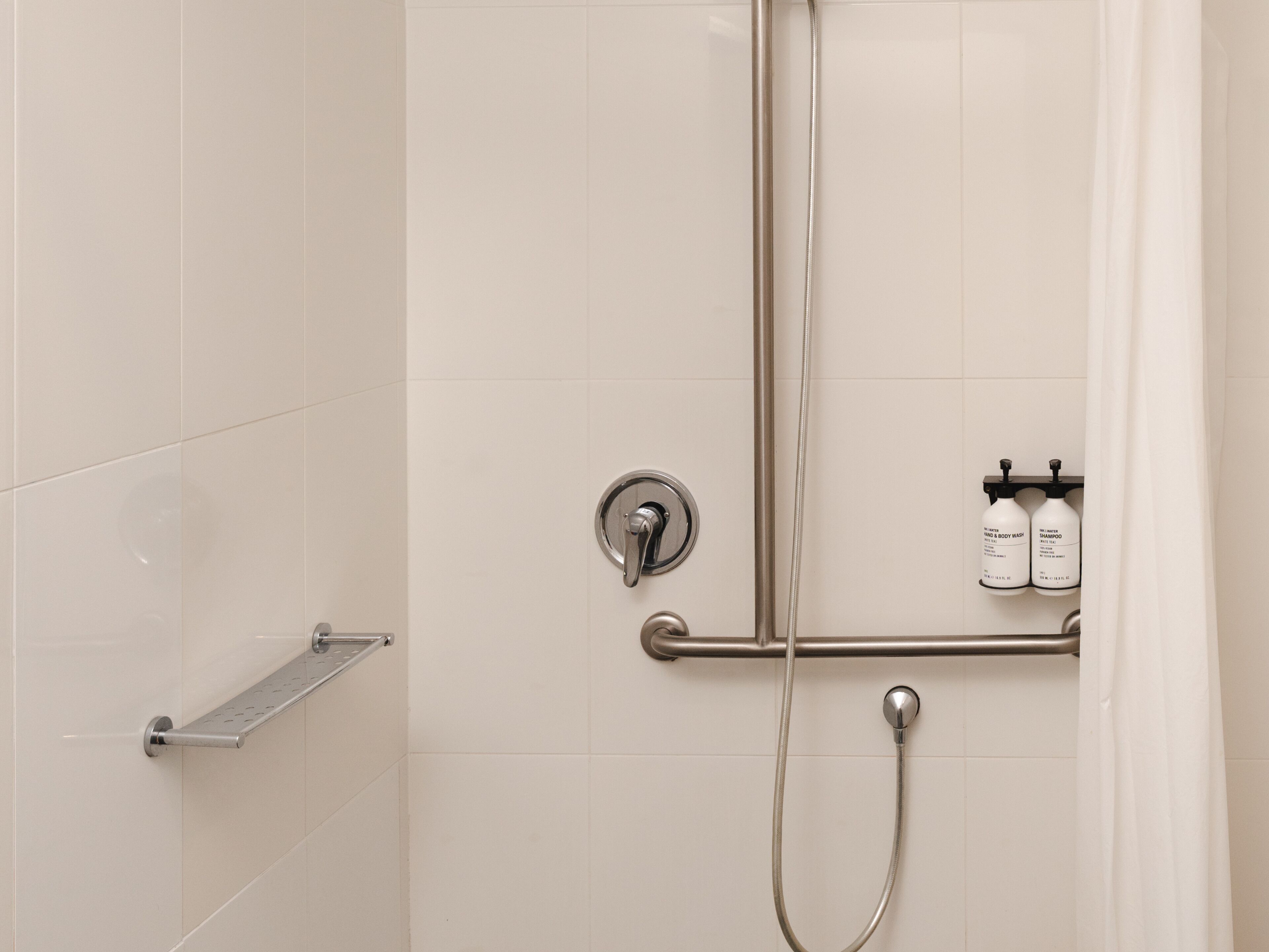 Une douche équipée d’un pommeau de douche à main, d’un robinet mural et d’un porte-serviettes avec des étagères pour les produits.