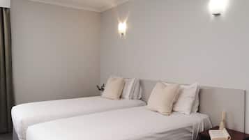 A hotel room with two single beds, a nightstand with a book and a candle, and a wall-mounted light fixture.