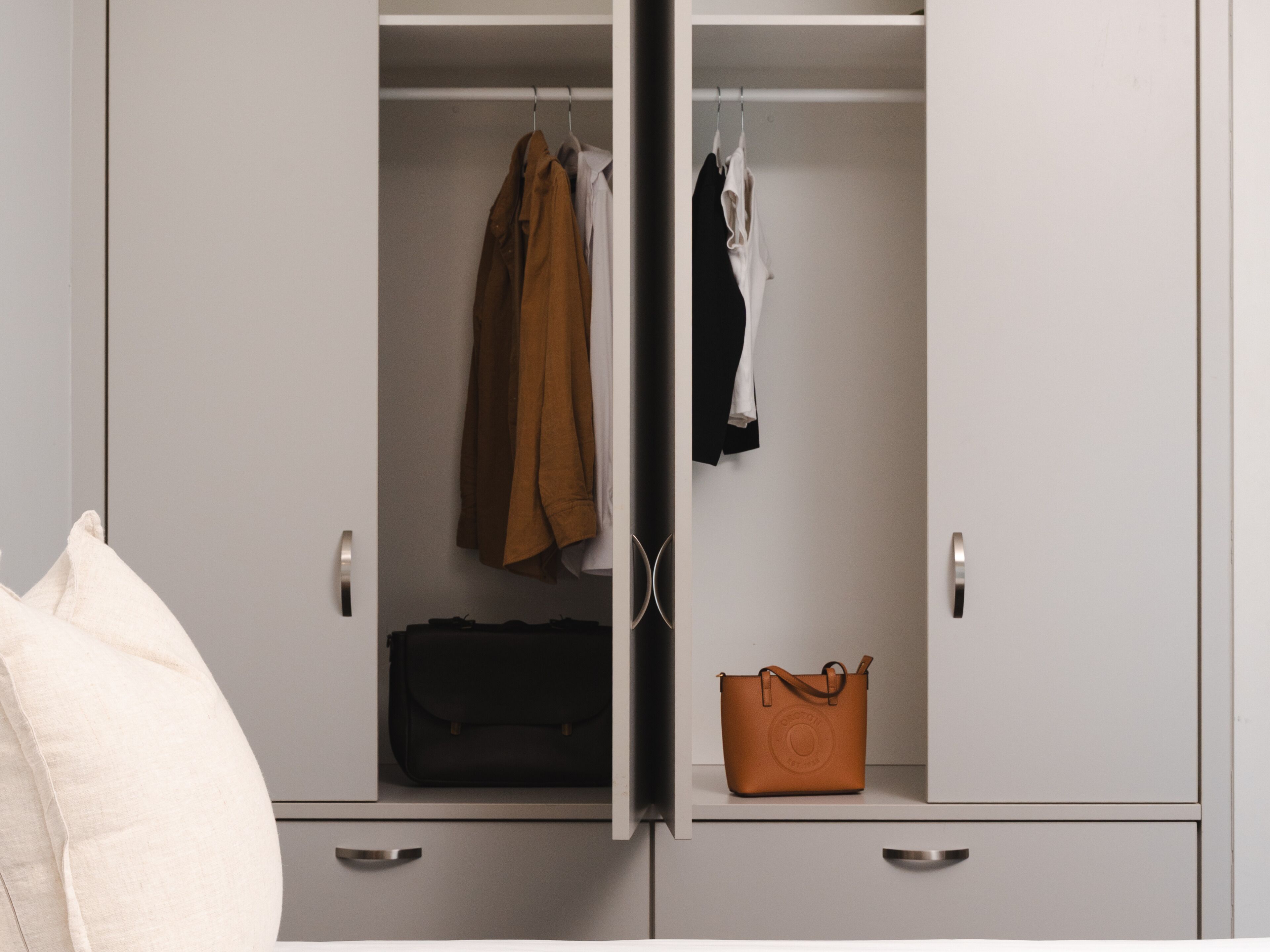 A wardrobe with hanging clothes, a black bag, and a brown bag.