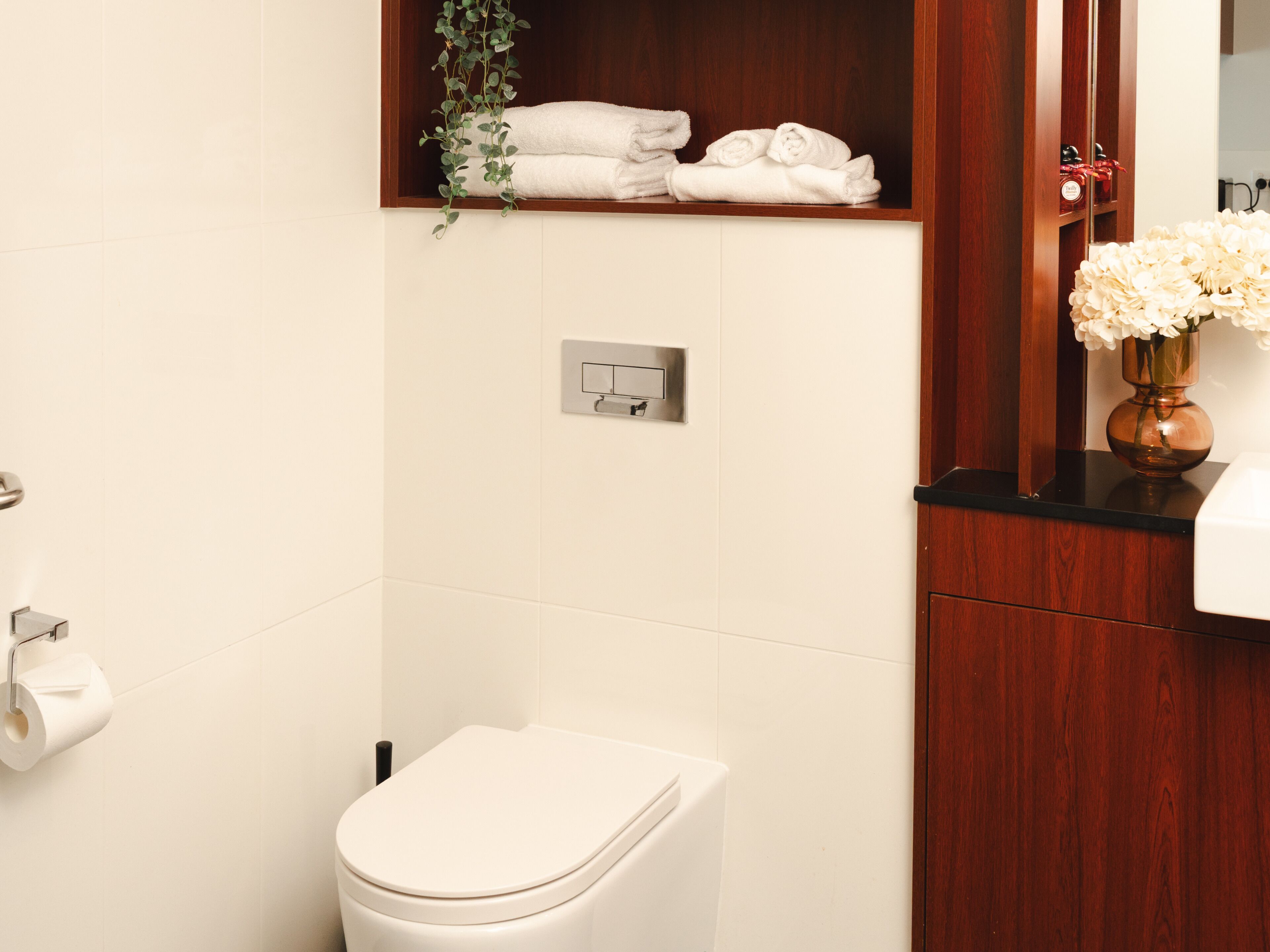 Une salle de bain comprenant des toilettes, un porte-serviettes avec des serviettes, un miroir et une plante.