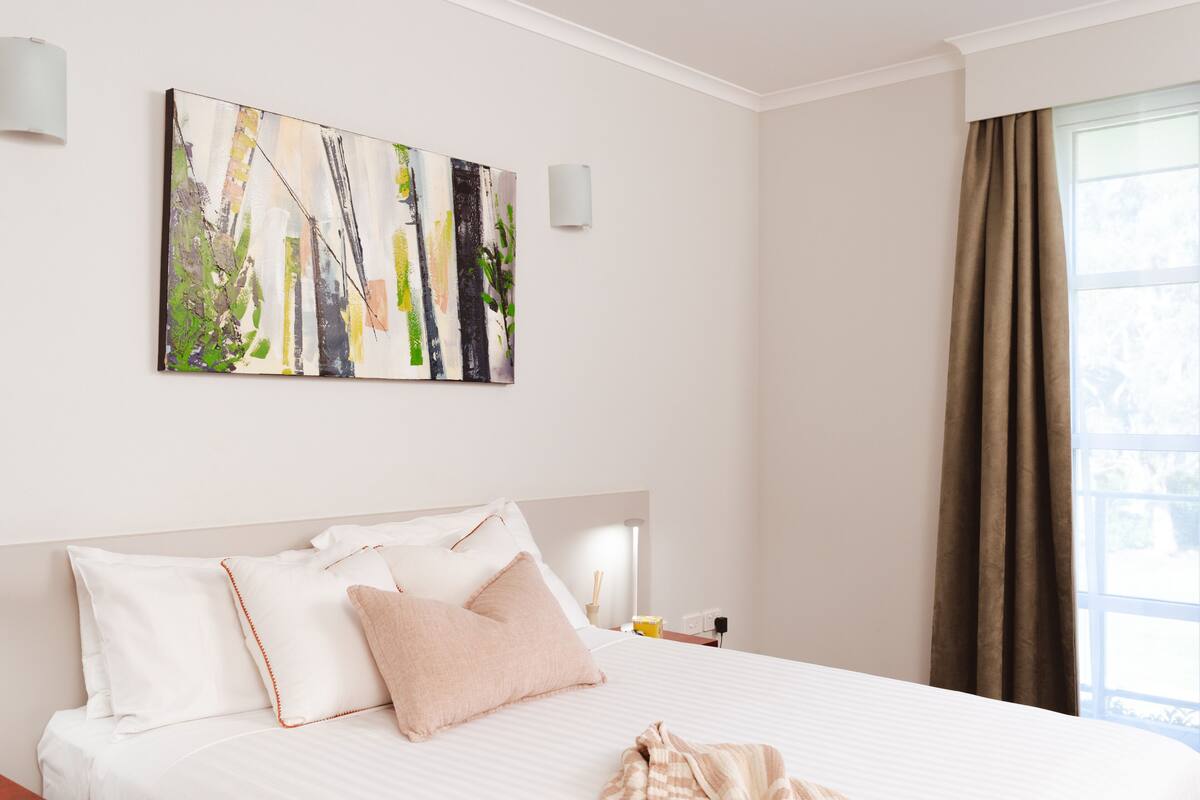 Una habitación de hotel con una cama grande, un cuadro en la pared y una ventana con cortinas.