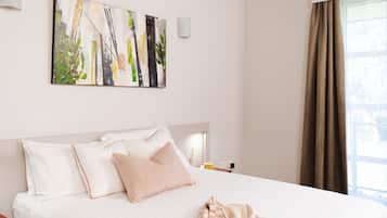 A hotel room with a large bed, a painting on the wall, and a window with curtains.