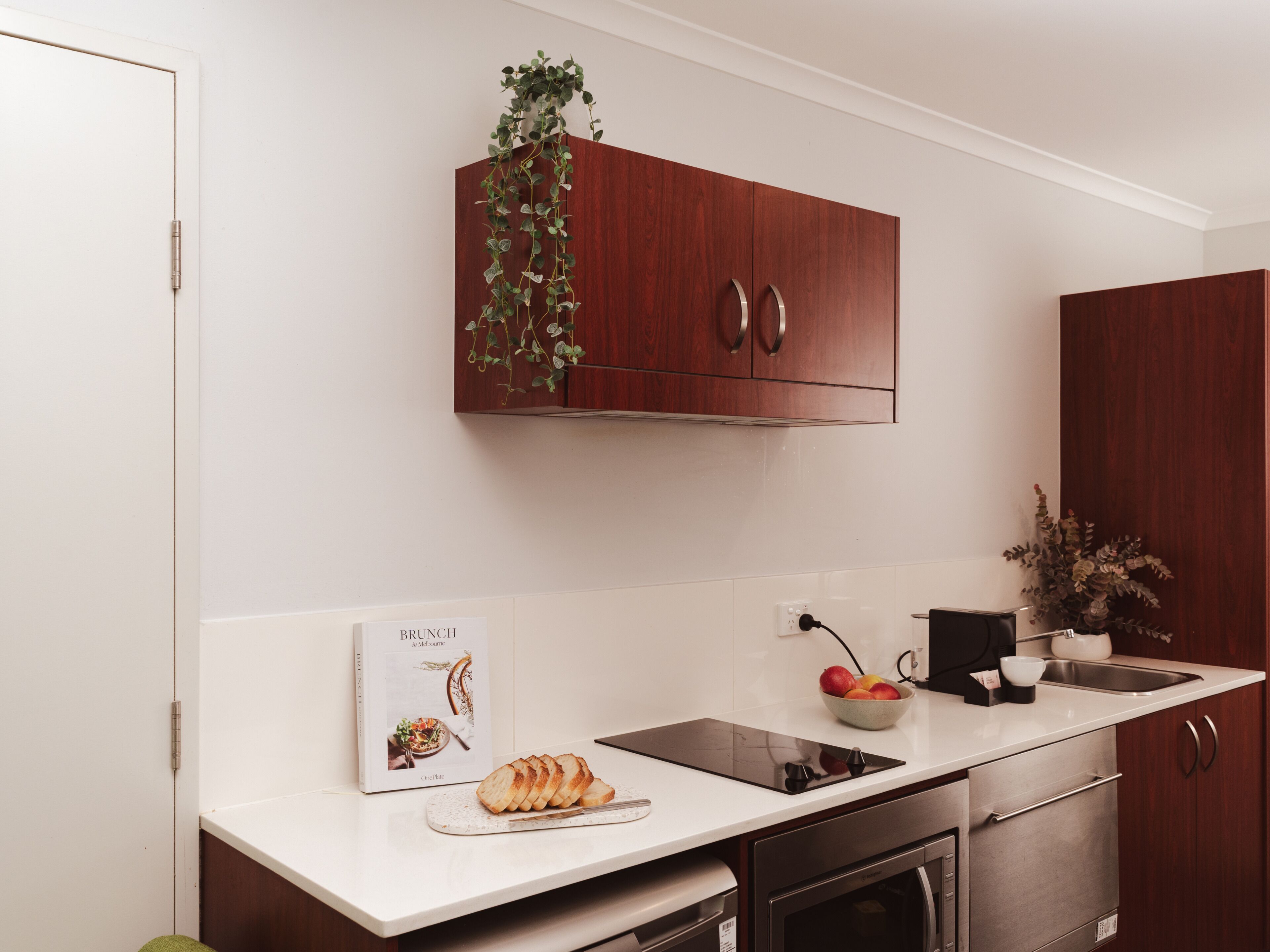 Una cocina moderna con encimeras blancas, armarios de madera, horno empotrado y un lavamanos.