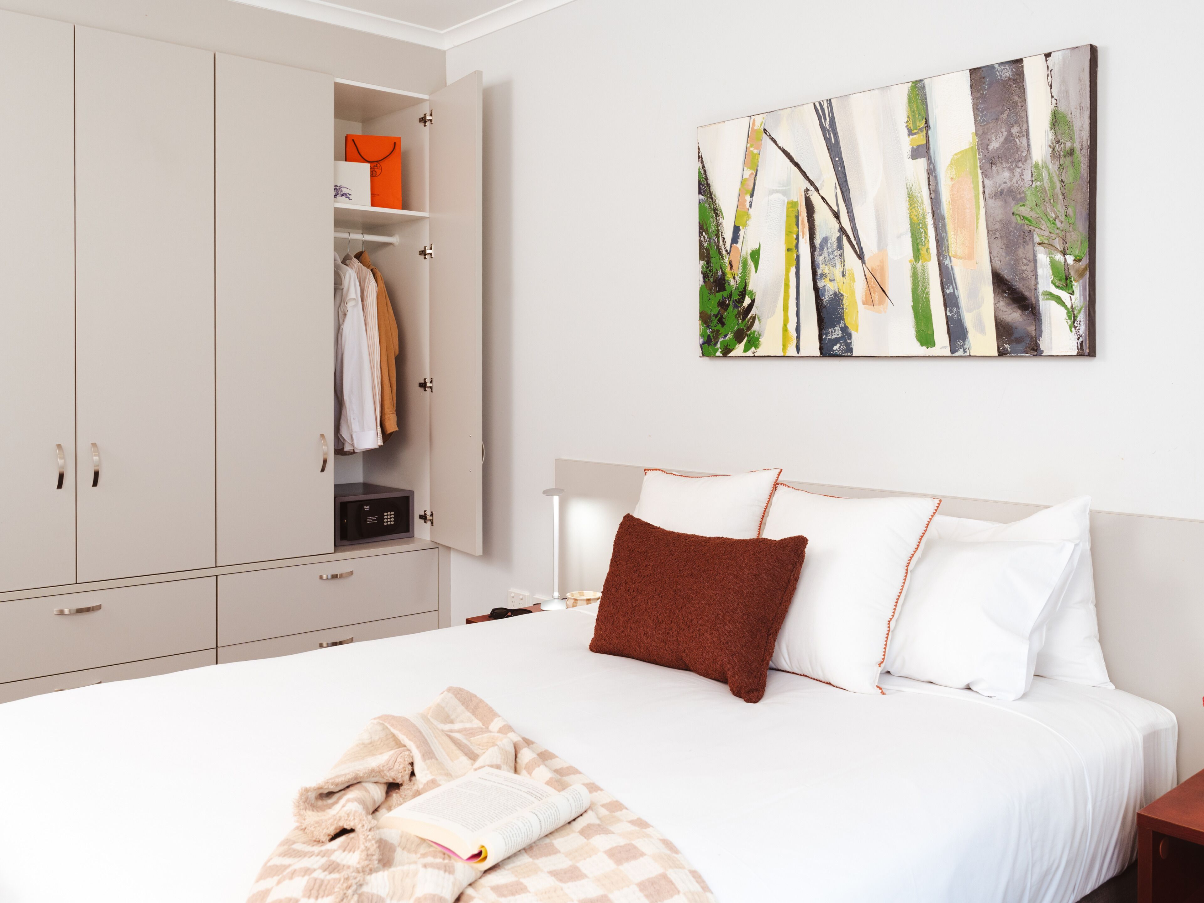 A bedroom with a bed, a wardrobe, and a painting on the wall.