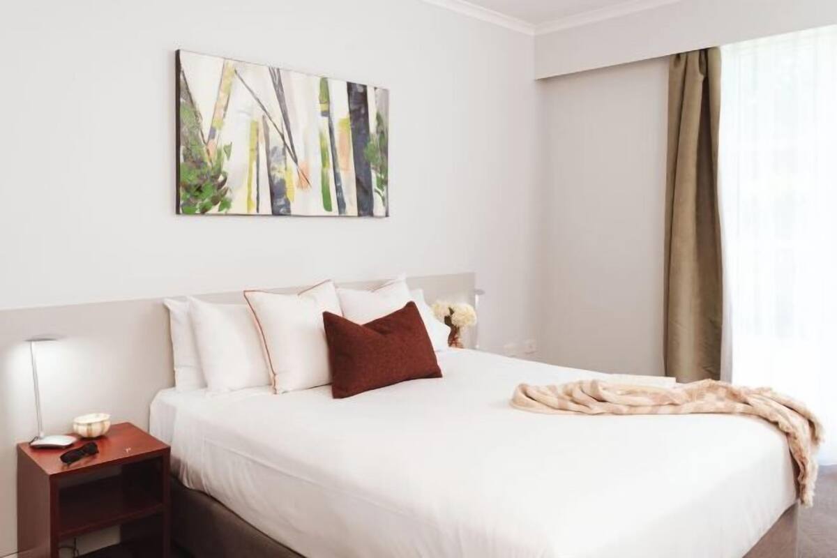 Una habitación de hotel con una cama, una mesita de noche, una lámpara y un cuadro en la pared.