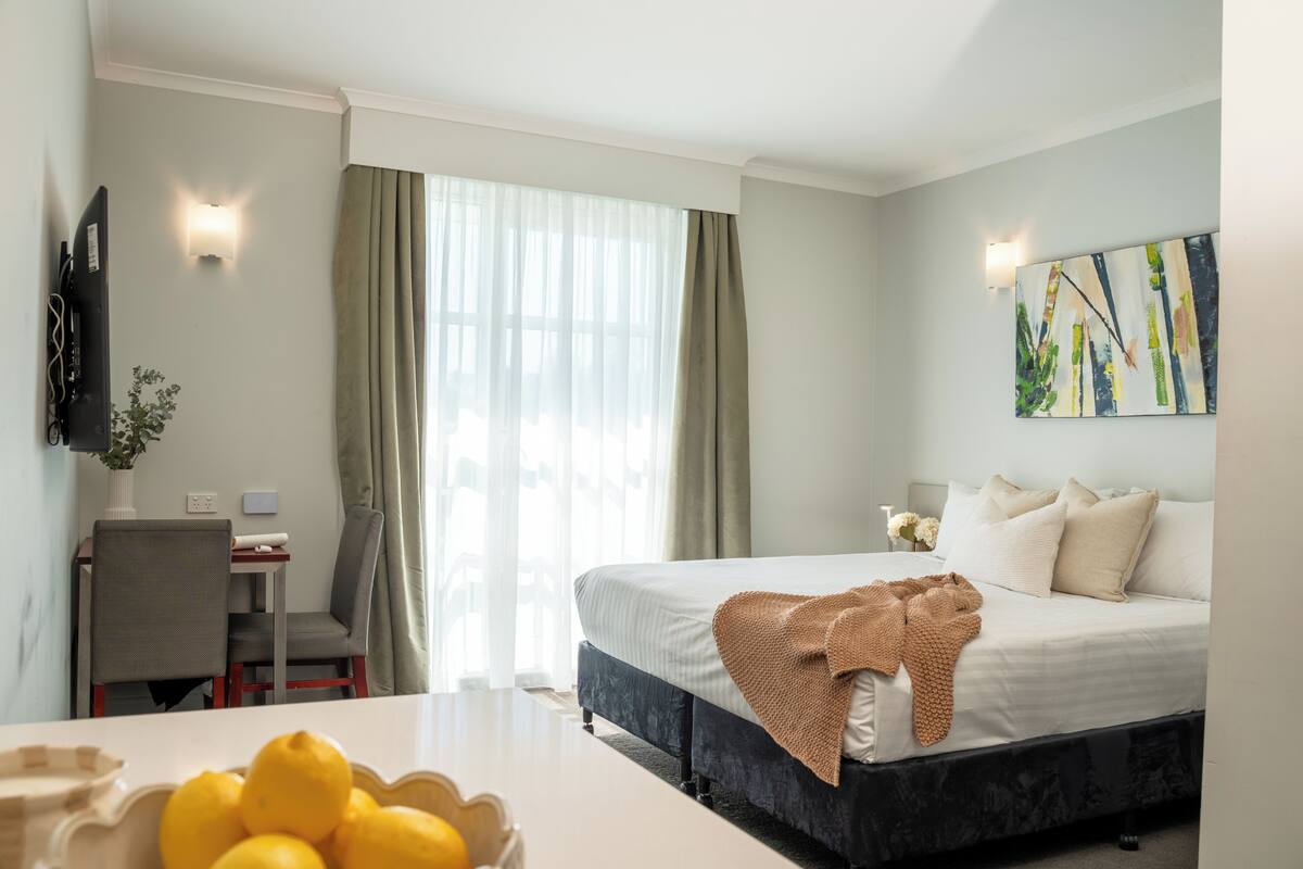 Una habitación de hotel con cama, escritorio, silla, televisor y un cuadro en la pared.