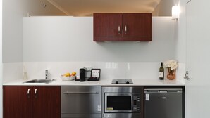 Cuina compacta amb forn integrat, microones i rentavaixelles, armaris de fusta i taulell blanc.