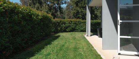 A modern building with a glass door, a well-maintained lawn, and a hedge.