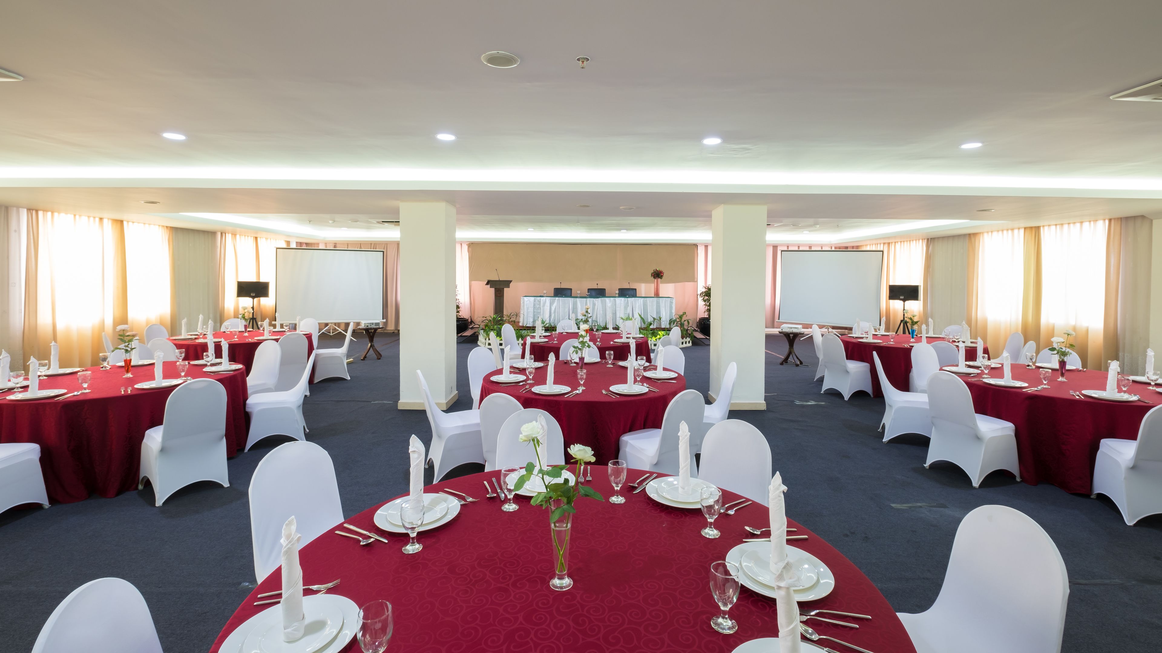 A conference room with round tables, white chairs, and red tablecloths.