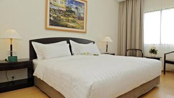 Una habitación de hotel con una cama grande, dos mesitas de noche con lámparas, un cuadro en la pared, una silla y una ventana con cortinas.