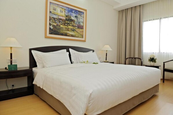 A hotel room with a large bed, two bedside tables with lamps, a painting on the wall, a chair, and a window with curtains.