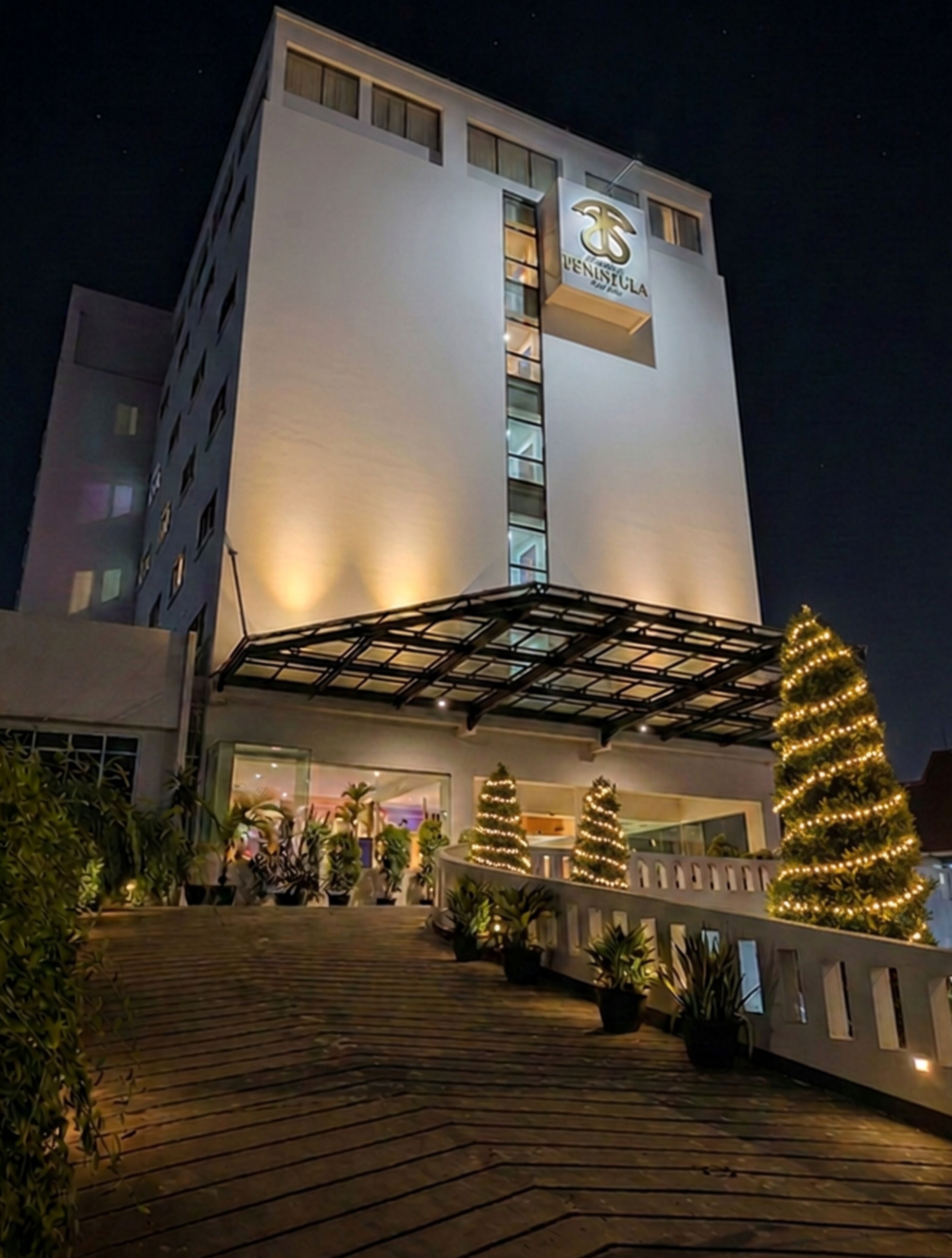 A hotel with a modern design, featuring a prominent entrance with a covered walkway and Christmas trees.